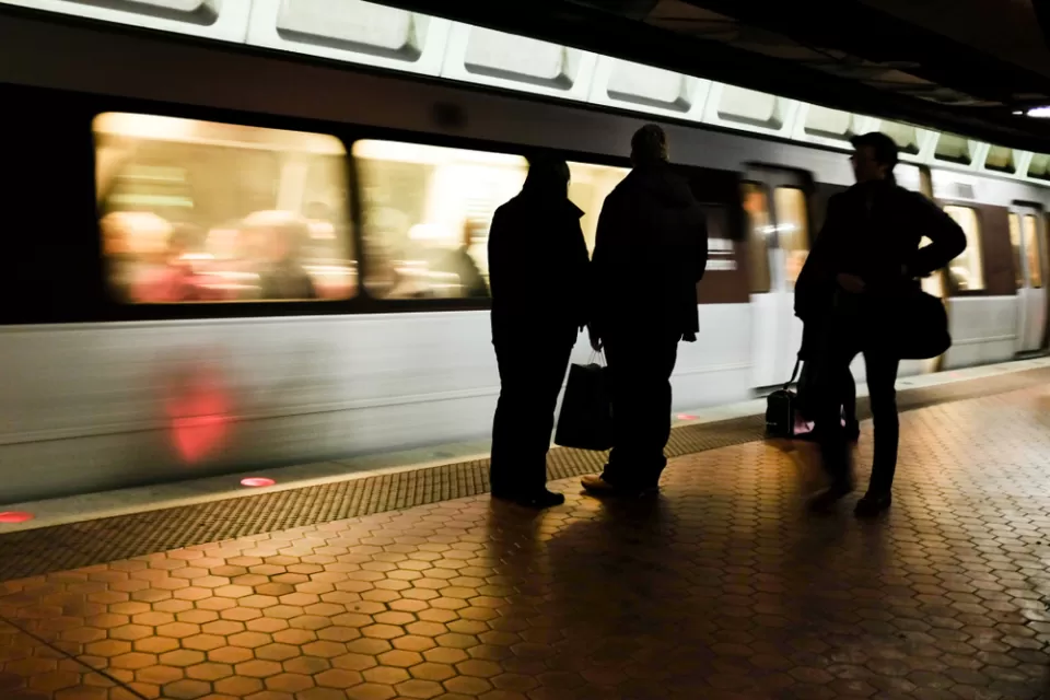 Three commuters on train platform sillhouetted against moving train